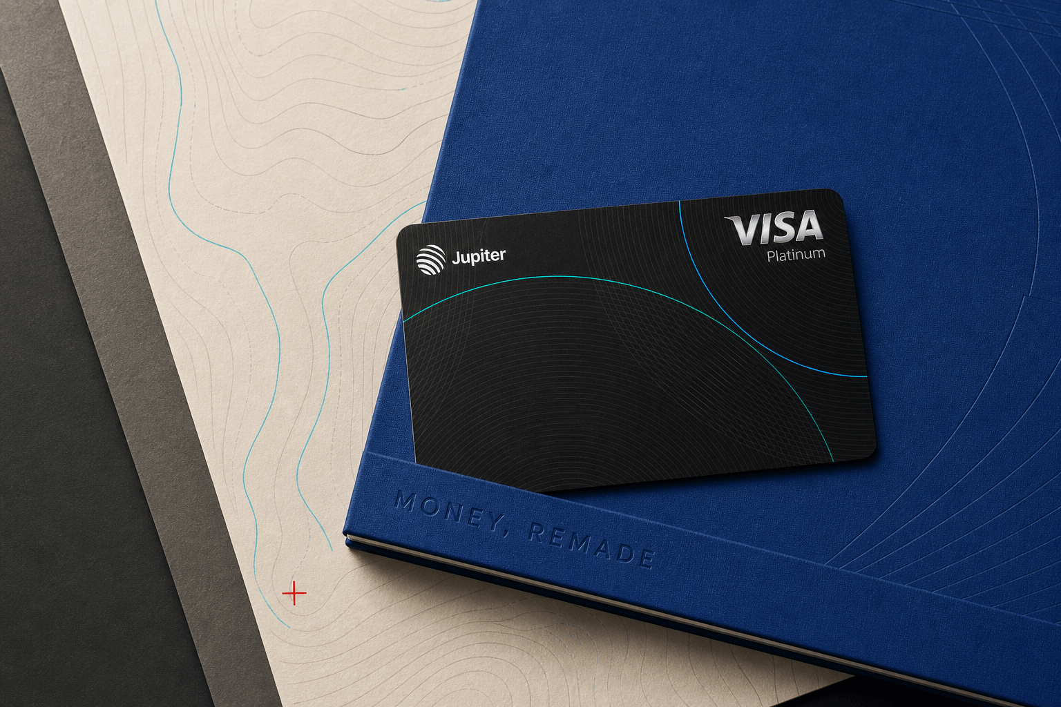 Jupiter Card resting across a cobalt atlas folio and ivory route map with a recessed Money, Remade wordmark